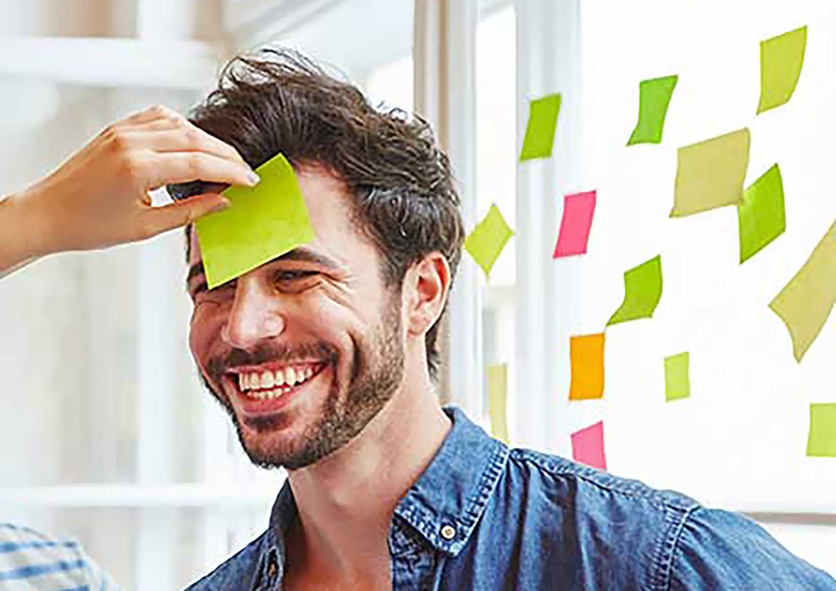 Ein Mann bekommt ein Post-It Zettel auf die Stirn geklebt (Workshops & Konferenzen zum Zukunftsunternehmen)